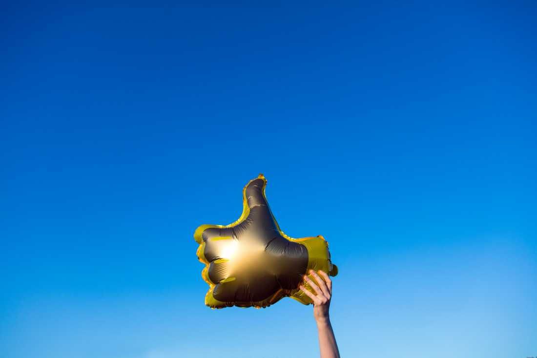 Golden thumbs up like balloon held in the air by a female hand against a bright summer sky