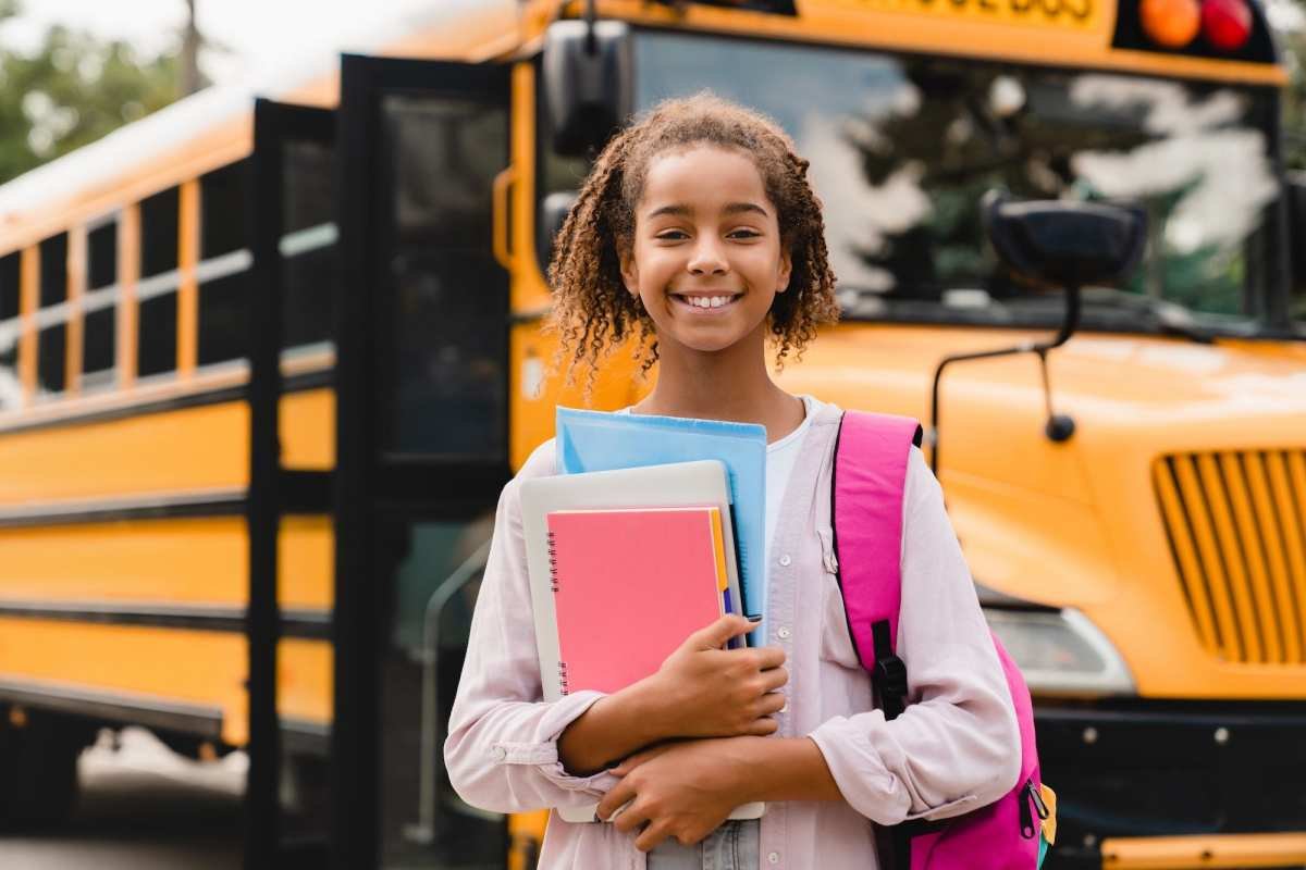 Colegiala afroamericana sonriente volviendo a la escuela con libros y cuadernos