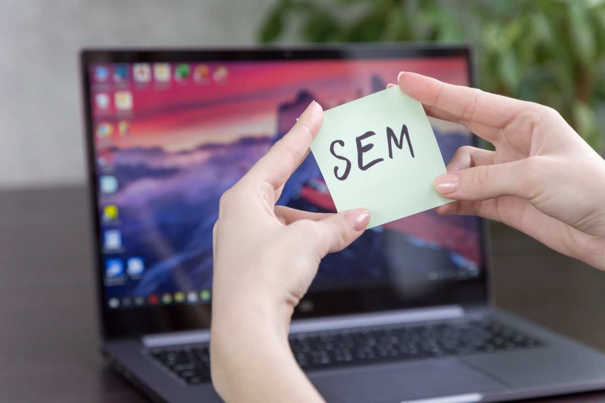 Inscripción SEM en una hoja de notas en manos femeninas en el fondo de una computadora portátil, enfoque suave