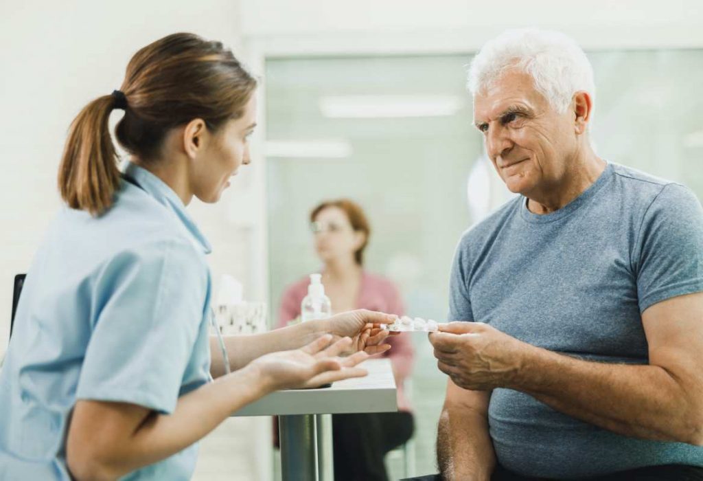 Enfermera cariñosa hablando con un hombre mayor en la sala de espera del hospital